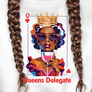 Puede incluir: Sudadera blanca con un diseño gráfico de una carta de reina. El diseño muestra a una mujer con gafas de sol en forma de corazón, una corona y una copa de vino. El texto "Queens Delegate" está debajo. Una persona sostiene una taza de café.