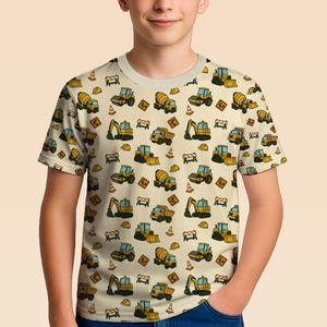 May include: A short-sleeved t-shirt with a repeating pattern of yellow and black construction vehicles, such as excavators and cement mixers, on a beige background. The design includes safety cones and road signs.