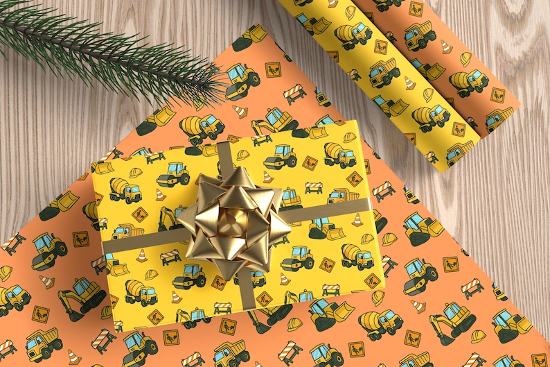 May include: A wrapped gift with a gold bow sits on orange and yellow wrapping paper. The paper is patterned with cartoon construction vehicles, including cement mixers, excavators, and dump trucks. A sprig of evergreen is in the corner.