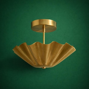 May include: A brass-coloured ceiling light with a ruffled, scalloped shade. The light has a circular base and a central rod connecting to the shade. The fixture is set against a dark green background.