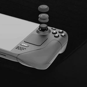 May include: A grey handheld gaming console with attached thumbsticks and spare thumbstick caps. The console has a screen, buttons, and a directional pad. The thumbstick caps are stacked above the console, ready to be fitted.