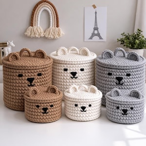 Pode incluir: Um conjunto de seis cestos de arrumação de croché em vários tamanhos e cores, incluindo castanho, branco e cinzento. Cada cesto apresenta um design de rosto de urso com detalhes bordados a preto e uma tampa a condizer. Para organizar itens.