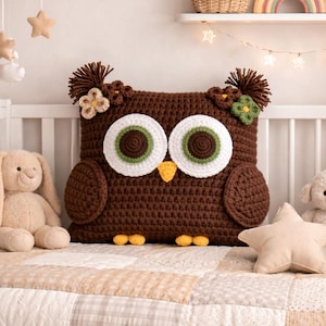 Könnte beinhalten: Ein braunes gehäkeltes Eulen-Kissen mit großen weißen und grünen Augen, einem gelben Schnabel und floralen Akzenten. Das Kissen liegt auf einer Patchwork-Steppdecke in einem Kinderbett, mit einem Stoffhasen und einem Lamm.