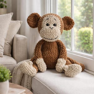 May include: A large, handmade crochet monkey in shades of brown and cream. The plush toy features a smiling face, large ears, and is seated on a window ledge. The monkey's body is a rich brown, with cream-colored accents on the face, hands, and feet.