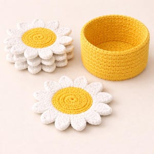 Könnte beinhalten: Gehäkelte Untersetzer in Form von weißen und gelben Gänseblümchen und ein gelber Häkelkorb. Die Untersetzer sind gestapelt. Der Korb ist zylindrisch.