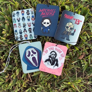 May include: Five rectangular air fresheners featuring horror movie characters. Designs include Michael Myers, Jason Voorhees, and Ghostface. The air fresheners are displayed on green grass.