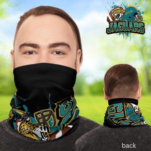 Puede incluir: Cubierta facial negra con un diseño en verde azulado, dorado y blanco con un jaguar, un balón de fútbol y un casco. El texto "JAGUARS" se muestra encima del diseño. También se ve la parte posterior de la cubierta facial.