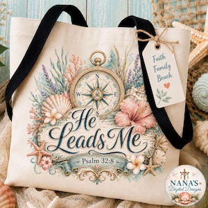 May include: A cream-colored canvas tote bag with black straps, featuring a compass, seashells, starfish, and hibiscus flowers. The text reads 'He Leads Me', 'Psalm 32:8', and a tag says 'Faith Family Beach'. A small circular logo is in the corner.
