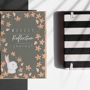 Può includere: Due diari su una superficie bianca. Uno ha una copertina grigia con un motivo floreale e il testo "WEEKLY Reflection journal". L'altro ha un motivo a righe bianche e nere.