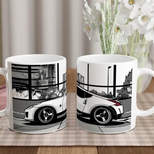 May include: Two white ceramic mugs featuring a black and white graphic illustration of a sports car parked in front of a building with large windows. The car design includes a white body, dark wheels, and a red taillight detail on the rear view.