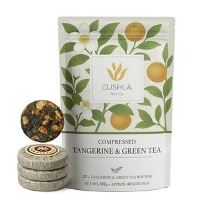 May include: A package of compressed tangerine and green tea rounds from Cushla Tea Co. The white package features illustrations of oranges, green leaves, and white flowers. The text "Compressed Tangerine & Green Tea" is printed on the package. The image also shows a tea cake and three tea rounds.