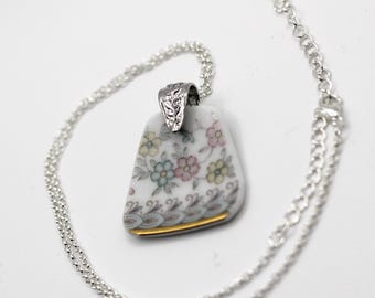 Pode incluir: Colar com pingente de porcelana branca com um design floral em cores pastel. O pingente é suspenso por uma delicada corrente prateada com uma argola de metal prateado. O pingente tem aproximadamente 3,8 cm de comprimento.