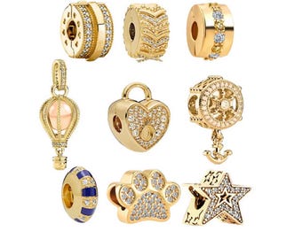 May include: A collection of gold-colored charm beads with various designs. The charms include a heart-shaped lock, a paw print, a star, a hot air balloon, and several round beads with decorative patterns and clear crystal accents.