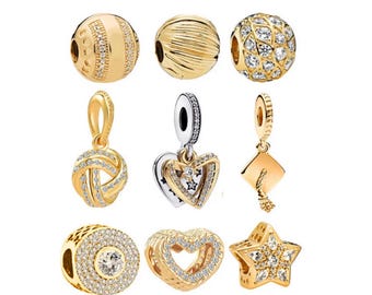 May include: A collection of gold-toned charms and pendants. The charms include various designs such as a beaded ball, a heart with star accents, a graduation cap, and a star-shaped charm, all adorned with sparkling details.