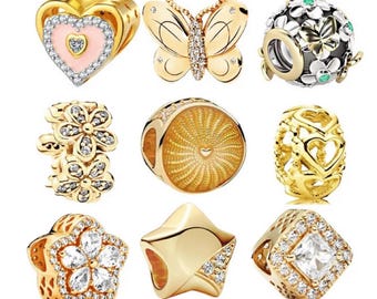 May include: A collection of gold-colored charm beads. Designs include a heart with a crown, a butterfly, a floral bead, a sunburst design, a bead with heart cutouts, a flower, a star, and a square with a clear stone.