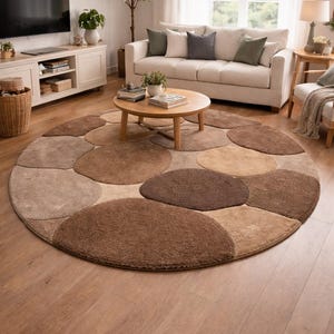 Könnte beinhalten: Runder Teppich mit Kieselsteinmuster in Braun- und Beigetönen. Der Teppich liegt auf einem Holzboden in einem Wohnzimmer. Der Durchmesser des Teppichs beträgt ca. 244 cm.