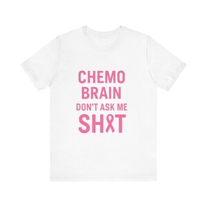 May include: White t-shirt featuring the pink text "Chemo Brain Don't Ask Me SH*T" and a pink ribbon symbol. A simple, casual top.