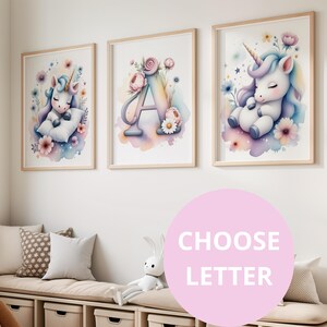 Peut inclure: Trois impressions encadrées à l'aquarelle. L'une représente une licorne, une autre la lettre « A » avec des fleurs, et la troisième une licorne endormie. Les impressions ont des couleurs pastel et des cadres en bois. Le thème est fantaisiste, adapté à une chambre d'enfant.