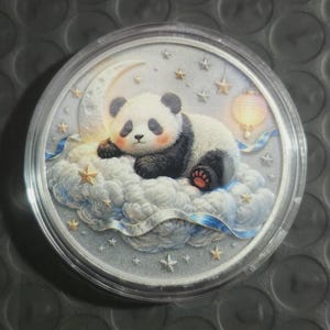 May include: A circular coin featuring a colored illustration of a panda resting on a fluffy white cloud. The scene includes a crescent moon, golden stars, and a hanging lantern against a starry night sky, all encased in a clear protective capsule.