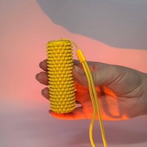 Peut inclure: Un rouleau de massage cylindrique jaune vif doté d'une surface texturée avec de nombreuses petites pointes. Le rouleau comprend une dragonne tissée jaune assortie fixée au sommet par un connecteur en plastique pour une prise en main sûre.