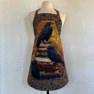 Może przedstawiać: Fartuch z motywem trzech czarnych kruków siedzących na stosie książek. Fartuch ma złote i granatowe tło ze wzorem wirowym. Kruki są szczegółowe z ciemnymi piórami.