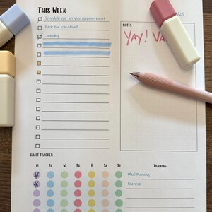 Pode incluir: Uma página de planejador branca com o texto "THIS WEEK" e caixas de seleção para tarefas. A palavra "Laundry" está destacada em azul. Uma caneta e um marcador rosa estão na página. As palavras "YAY! VA" estão escritas em rosa.