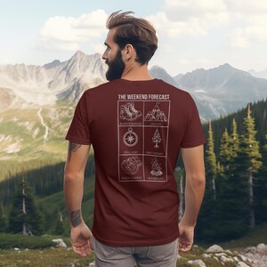 Peut inclure: T-shirt bordeaux avec l'inscription "THE WEEKEND FORECAST" et des icônes blanches. Les icônes représentent des chaussures de randonnée, des montagnes, une boussole, un arbre, un sac à dos et un feu de camp. Vêtement décontracté.