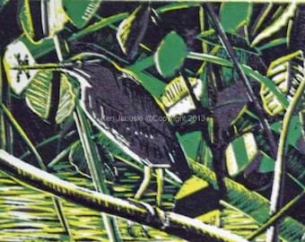 May include: A black and green linocut print of a bird perched on a branch. The bird is surrounded by green and yellow foliage. The print is signed "Ken Januski @ Copyright 2013".
