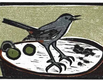 May include: A black and white woodblock print of a gray bird with a long tail standing on a round dish with black and white markings. The bird has a long beak and is looking to the right. The dish has a brown rim and is filled with small black and white dots.