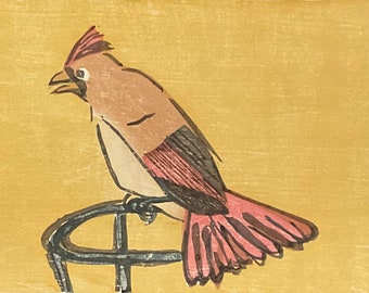 May include: A brown and pink bird with a red crest perched on a black metal stand against a yellow background.