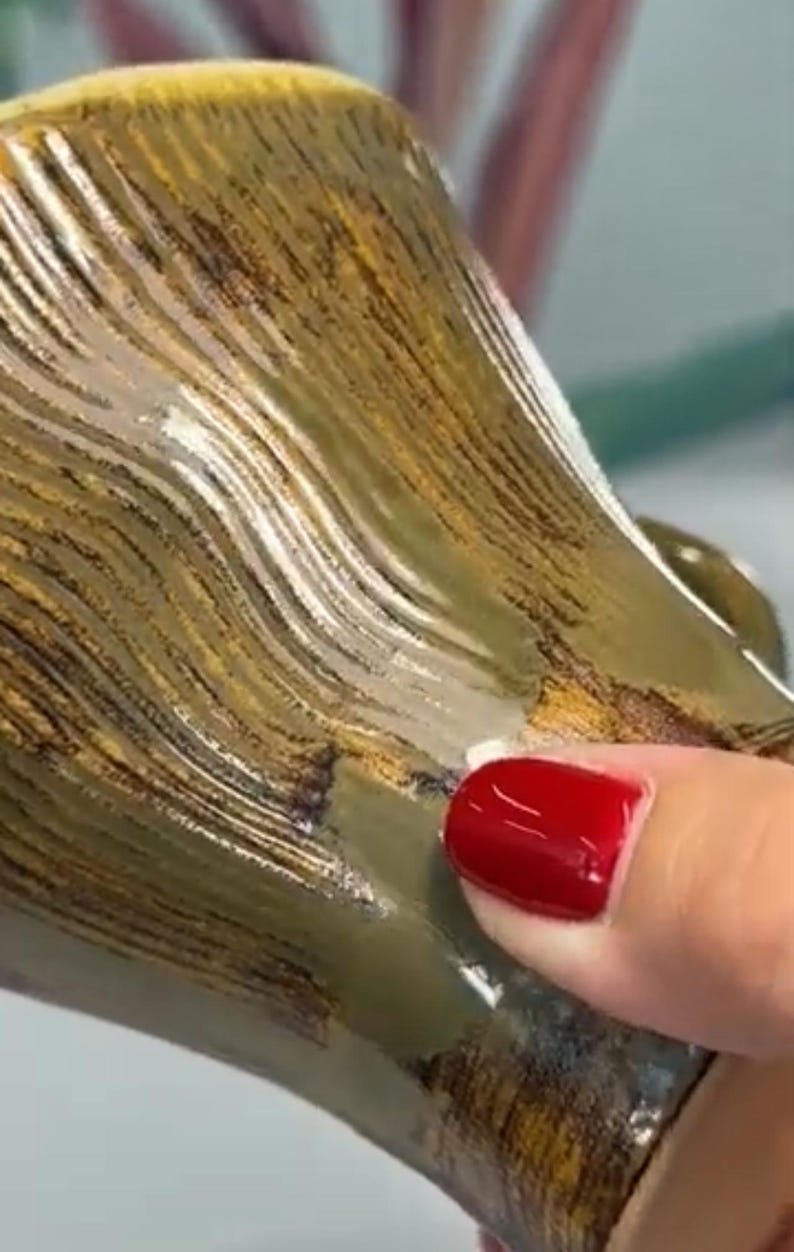Puede incluir: Primer plano de una taza de cer&aacute;mica con un patr&oacute;n texturizado en forma de olas en tonos marr&oacute;n, dorado y verde. La superficie de la taza tiene un acabado brillante. Una mano con esmalte de u&ntilde;as rojo toca la taza.