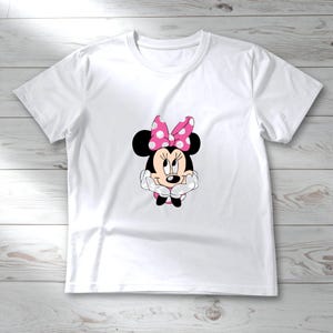 May include: White t-shirt featuring a graphic of Minnie Mouse. Minnie Mouse is depicted with black ears, a pink polka-dot bow, and a smiling face. The shirt is made of a soft, lightweight material, perfect for casual wear.