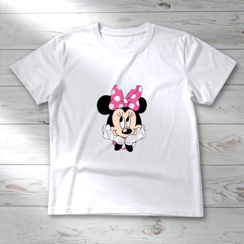 May include: White t-shirt featuring a graphic of Minnie Mouse. Minnie Mouse is depicted with black ears, a pink polka-dot bow, and a smiling face. The shirt is made of a soft, lightweight material, perfect for casual wear.