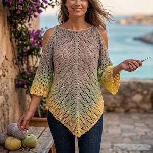 May include: A crocheted top with open shoulders, featuring a gradient of colors from gray to yellow. The top is paired with dark blue jeans. A crochet hook and yarn balls are on a wooden surface.