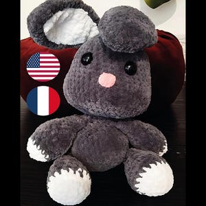 Peut inclure: Une peluche lapin grise faite à la main, avec des accents blancs sur les oreilles et les pieds. Le lapin a des yeux noirs en forme de bouton et un nez rose. La peluche est douce et câline.