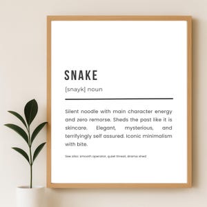 Może przedstawiać: Oprawiony wydruk z napisem "SNAKE" w czarnym kolorze. Poniżej definicja opisująca węża jako "cichy makaron". Jasna drewniana rama pasuje do nowoczesnych wnętrz.