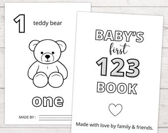 May include: Two white flashcards with black text and illustrations. One card features the number 1, a teddy bear illustration, and the word "one". The other card says "BABY'S first 123 BOOK" with a heart and text "Made with love by family & friends."