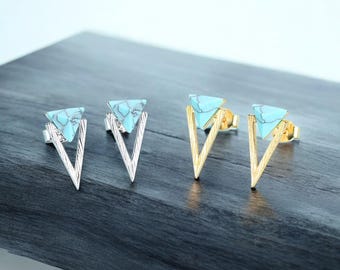 Könnte beinhalten: Zwei Paar Ohrstecker, eines in Silber und eines in Gold. Jeder Ohrring hat einen türkisfarbenen Dreiecksstein, der in einem V-förmigen Rahmen gefasst ist. Die Ohrringe werden auf einer dunkelgrauen Oberfläche präsentiert.