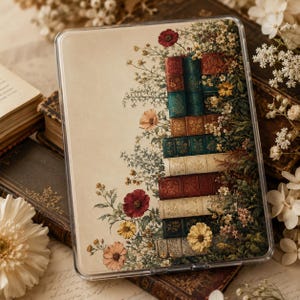 May include: A clear protective tablet case featuring a printed illustration of a vertical stack of antique books surrounded by colorful wildflowers, including red poppies, yellow daisies, and small white blossoms on a cream-colored background.