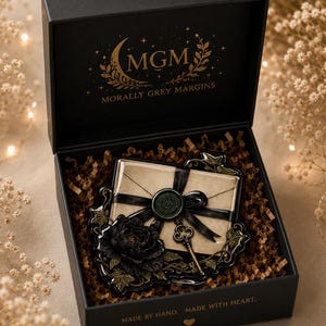 May include: A black gift box containing a decorative envelope with a green wax seal, a black ribbon, a small metal key, and a black flower. The box lid features gold text reading MGM MORALLY GREY MARGINS and the base reads MADE BY HAND. MADE WITH HEART.