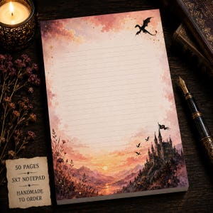 May include: A 5x7 notepad with 50 pages featuring a watercolor illustration of a sunset landscape with a castle, flying dragons, and wildflowers. The paper has horizontal lines for writing and a small tag stating 50 PAGES 5X7 NOTEPAD HANDMADE TO ORDER.