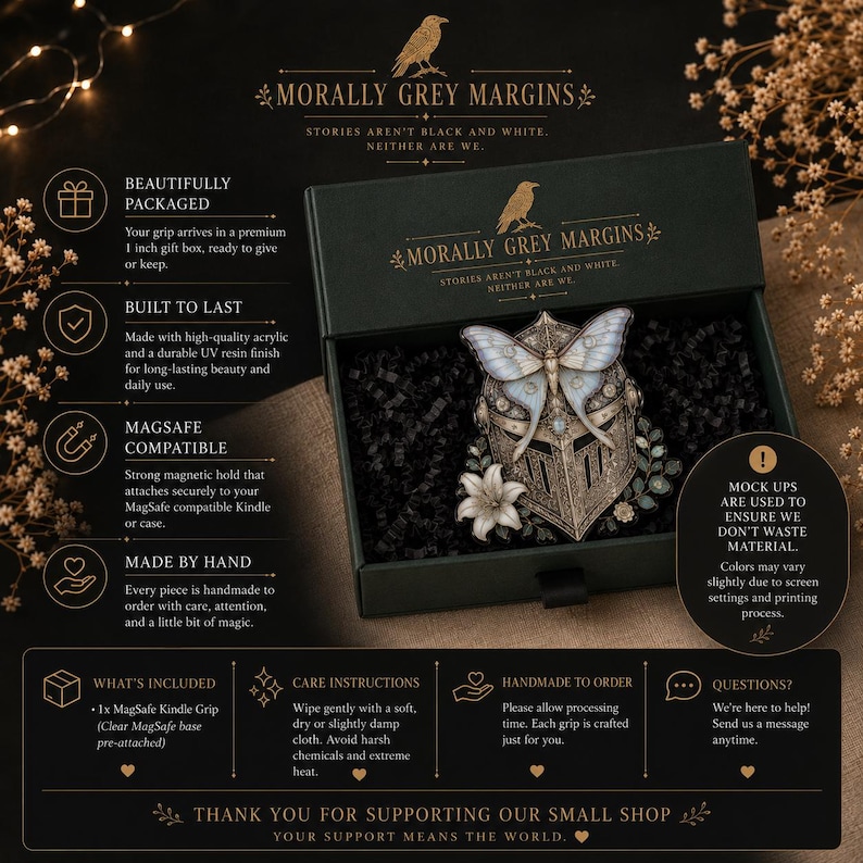 May include: A black gift box containing a MagSafe grip featuring a metallic knight helmet adorned with a large white moth and a white lily. The box lid displays the text Morally Grey Margins and Stories Aren't Black and White, Neither Are We.