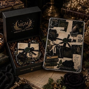 May include: A black gift box with the gold text MGM MORALLY GREY MARGINS containing a decorative envelope with a wax seal and key, alongside a rectangular tray featuring a collage of vintage letters, black roses, butterflies, and books.