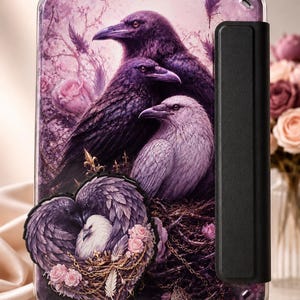 May include: A rectangular tablet case featuring a purple-toned illustration of three ravens perched together amidst roses. A heart-shaped emblem at the bottom displays two ravens nesting with a white bird, accented by gold chains and pink roses.