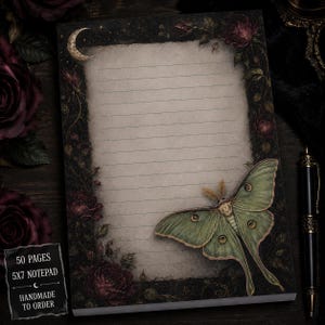 May include: A 5x7 inch notepad with 50 pages featuring a lined, parchment-style center. The border is decorated with dark red roses, a golden crescent moon, and a large, detailed green luna moth resting on the bottom right corner.