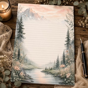May include: A rectangular sheet of stationery paper featuring a printed landscape illustration of a mountain range, a flowing river, and evergreen trees. The paper has horizontal lines for writing and is decorated with soft pink and green floral accents.