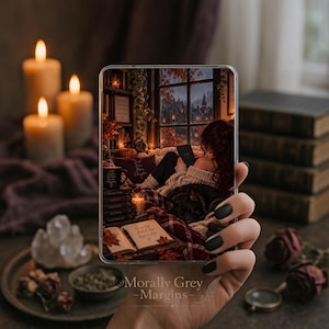 May include: A clear rectangular phone case featuring a printed illustration of a cozy room with a person reading by a window, surrounded by books, candles, and autumn leaves. The design includes a stack of books and an open journal with handwritten text.