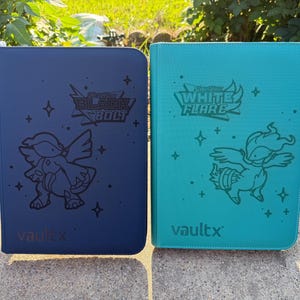 May include: Two card binders, one navy blue and one teal, are displayed side-by-side. The navy binder features the text "Black Bolt" and a cartoon character. The teal binder has "White Flare" and a similar character. Both have the brand name "vaultx".