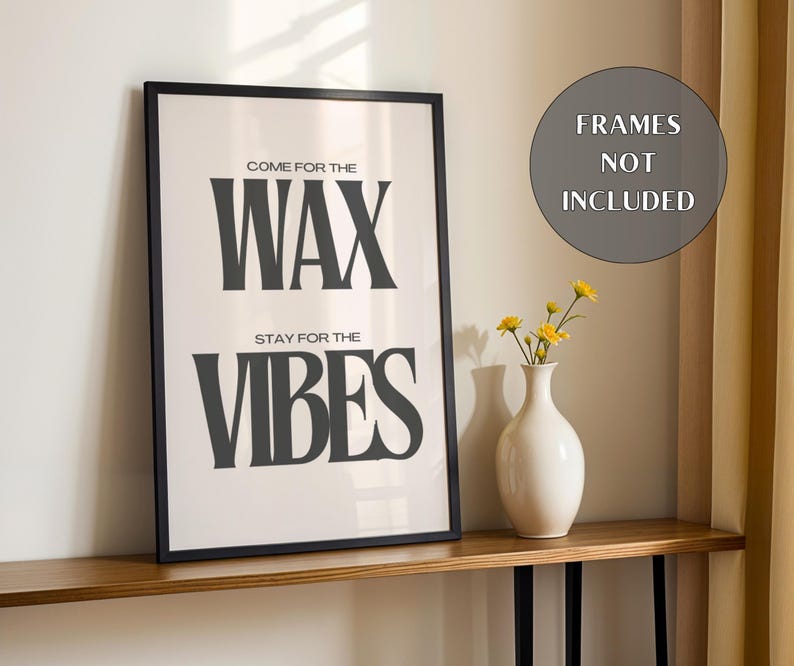 Puede incluir: Un cuadro rectangular con marco negro que presenta el texto COME FOR THE WAX STAY FOR THE VIBES en letras negras en negrita sobre un fondo blanco. Un jarr&oacute;n de cer&aacute;mica blanca con peque&ntilde;as flores amarillas se sit&uacute;a junto al cuadro.
