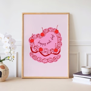 以下が含まれることがあります： 赤いさくらんぼと手書き風の「happy nail day!」の文字が入った、ハート型のケーキのデザインが特徴の、額入りのピンクのアートプリント。ケーキには装飾的なボーダーがあり、明るいピンクの背景に配置されています。